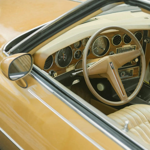 Interior view of a classic car with tan leather seats, wood panel dashboard, and chrome accents