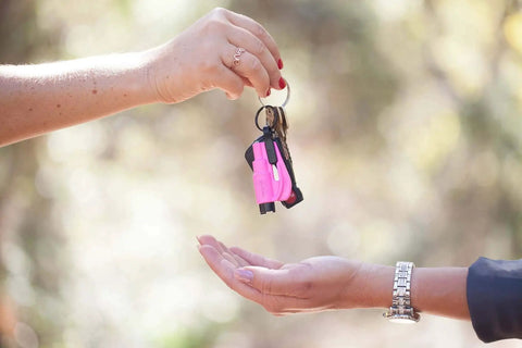 Hands exchanging a pink keychain with Pack Of 2 Emergency Car Escape Tools With 2 In 1 Seatbelt Cutter And Window Breaker Pink Keychain.