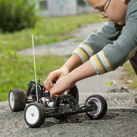 Child adjusting RC car outdoors on a paved surface, focusing on mechanical parts and wiring for precision modeling.