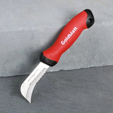 Stainless Steel Roofing And Flooring Knife Soft Grip For Carpet And Linoleum with serrated blade and red handle on stone surface.