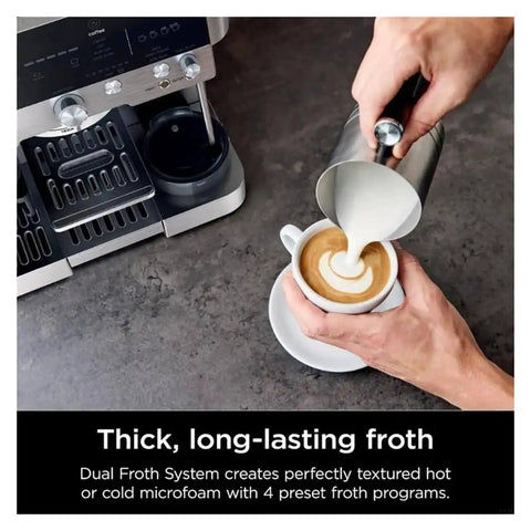 Person using metal frothing pitcher to pour milk into coffee next to espresso machine on counter.