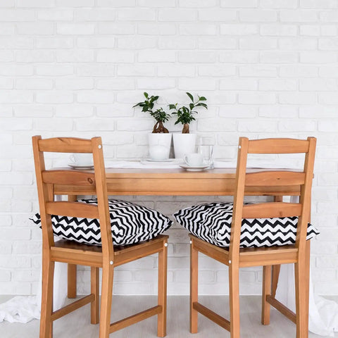 Dining area with wooden table and chairs, white brick wall, decorative plants, and chevron-patterned cushions on the chairs