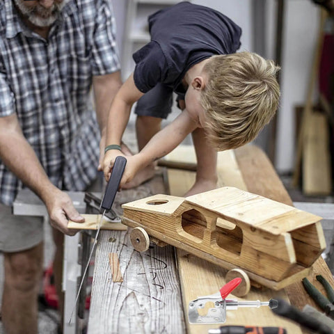 Child using a saw on a wooden toy car with Four Pack Horizontal Toggle Clamps With Push Pull Quick Release For Workholding visible on the table.