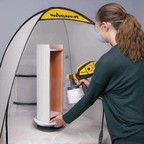 Woman using a spray gun inside a tent with a Revolving Paint Spray Turntable With 11 Inch Round Platform For Spray Painting Projects And Crafting Smooth 360 Degree Rotation For Accessing Every Angle On Miniatures Lamps Bird Houses Models And More.