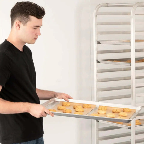 Person holding Pro Grade Aluminum Baking Sheet Pan For Oven 18 Inch Long By 26 Inch Wide By 1 Inch Deep Cookie Sheet 12 Pack with cookies.