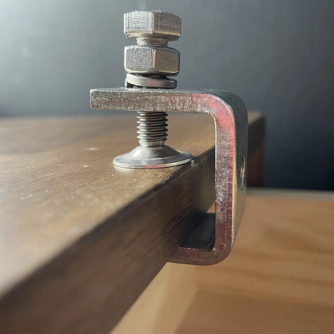 Front view of a red-painted steel C-clamp securing a wooden board edge; 1-inch jaw with screw and pad