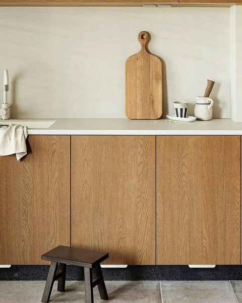 Kitchen setting with Adhesive Touchless Foot Pull for Cabinet Trash Cans, Silvery Finish, visible under wooden overlay cabinet doors.