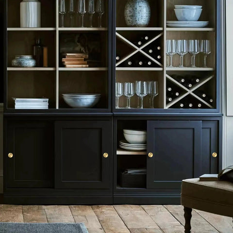 Black cabinet with 4 Pack Solid Brass Finger Pulls For Sliding Doors And Cabinets in brushed gold, showcasing glassware and decor.