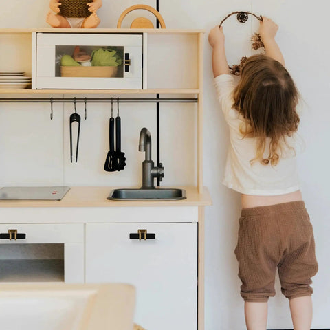 Child reaching in play kitchen with black T Bar handles on cabinets and drawers, modern cupboard hardware visible.