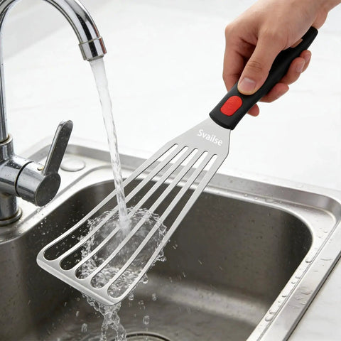 Flexible Stainless Steel Fish Spatula With Silicone Handle Slotted Turner being washed under running water in kitchen sink.