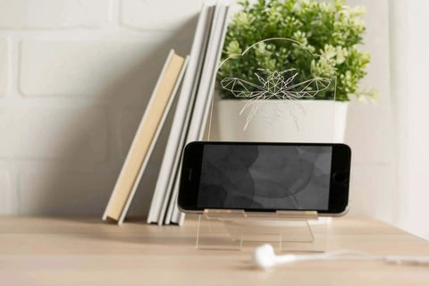 Smartphone on a stand with books and a plant in the background, placed on a wooden desk.