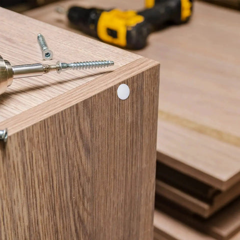 Four Sizes White Plastic Hole Plugs For Cabinet And Furniture installed on wooden surface, covering screw hole next to drill.