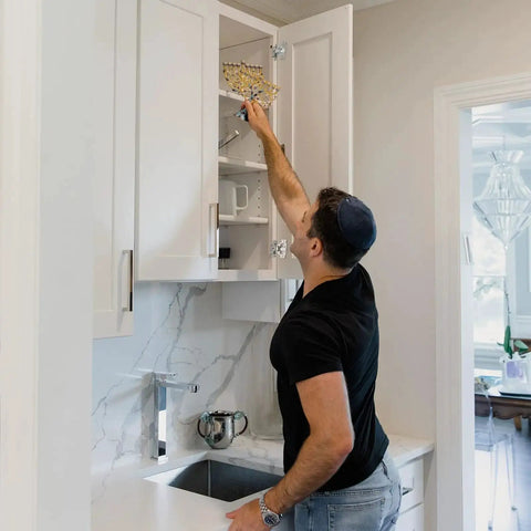 Person reaching into a kitchen cabinet using the Fifty Piece One Half Inch Overlay Soft Close Concealed Cabinet Hinge Set For Face Frame Doors.