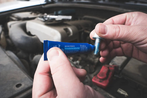 Person holding tube of Blue Medium Strength Threadlocker That Eliminates Vibration No Drip Seals Leaks Prevents Rust And Disassembles Without Cracking Or Shrinking Permatex 27 070 6 Ml and a bolt in a vehicle engine bay.