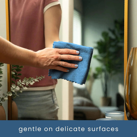 Person cleaning a mirror with a blue towel from 50 Pack Microfiber Towels 11.8x11.8 In Lint-Free Reusable For Home And Car