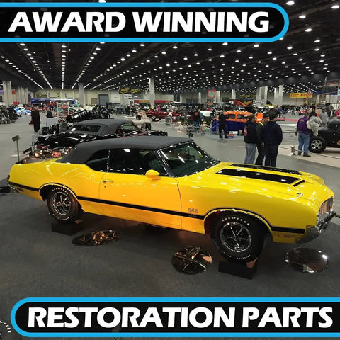 Side view of a yellow classic muscle car on display at an auto show, restoration parts banners visible in background.