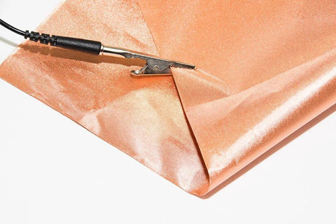 Grounding cable with black cord and metal alligator clip on orange velvet fabric background