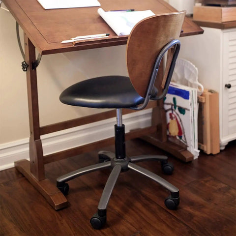 Office chair with black seat and wooden backrest, placed near a drafting table on a wooden floor in a home office setting.