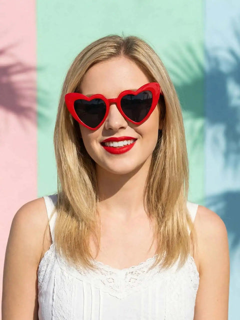 Unisex Heart Shaped Full Frame Sunglasses With Multicolor Red Frame And Gray Lenses UV400 Protection For Bold Everyday Versatile Sunwear And Trendy Casual Looks worn by a smiling woman against a colorful background.