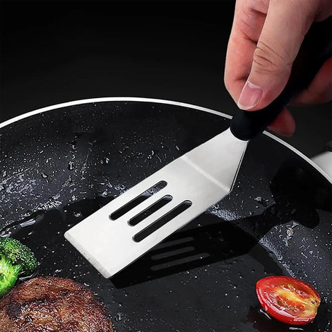 Hand holding a slotted spatula flipping food in a pan, part of Two Piece Small Metal Spatula Set For Kitchen Use Stainless Steel Slotted And Solid Mini Spatulas.