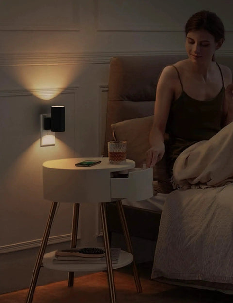 Plug In Night Light 2 Pack Dusk To Dawn Sensor Dimmable 3000K Vintage Black installed beside bed with glowing light.