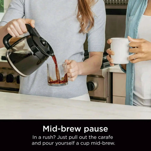 Person pouring coffee from a 12-cup programmable coffee maker with glass carafe into a cup, showcasing mid-brew feature.