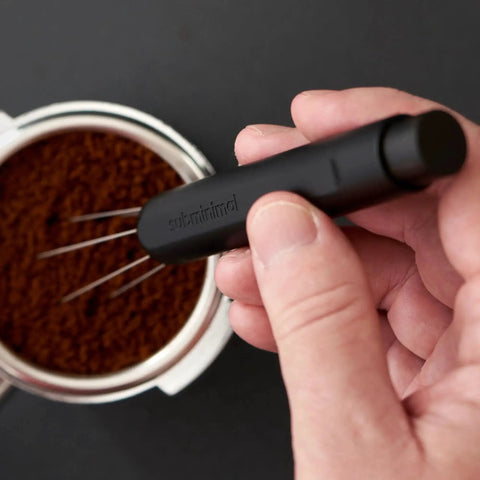 Subminimal Flick WDT espresso distribution tool in black held above a portafilter filled with ground espresso.