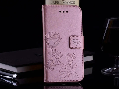 Pink floral embossed leather phone case standing upright on a table next to a glass, pen, and notebook.