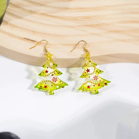 Christmas tree-shaped earrings with festive green and red accents on a wooden background