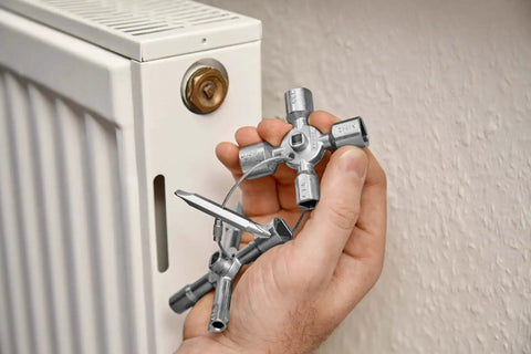 Hand holding TwinKey Multifunctional Spanner Kit With Magnetic Eight Arm Two By Four Way Spider Keys in front of radiator valve