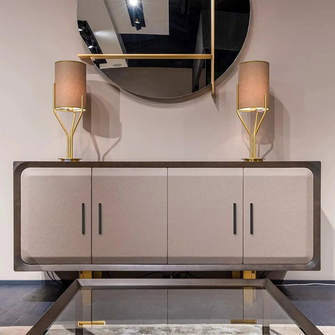 Modern sideboard with matte black cabinet handles, adorned with two gold lamps, reflecting in a round mirror above.