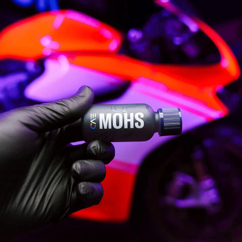 Gyeon Mohs Ceramic Coating Kit For Cars DIY Deep Gloss And 3 Year Protection bottle held in hand, motorcycle in background
