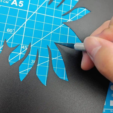 Using a carving knife from the Complete 42Pcs 3D Printer Nozzle Cleaning Tool Kit on black paper over blue cutting mat.