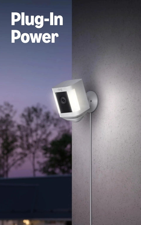 Spotlight Cam Plus Battery Security Camera With HD Video Color Night Vision plugged into exterior wall at dusk.