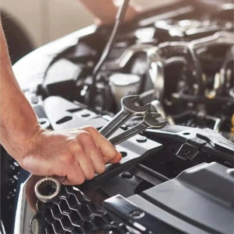 Mechanic using wrenches to work on car engine under the hood in a garage setting