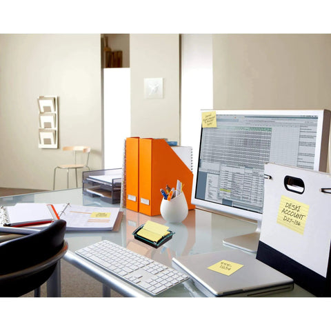Pop-up sticky note dispenser with one 50-sheet canary yellow 3 in x 3 in pad, black base and clear lid, on office desk setup