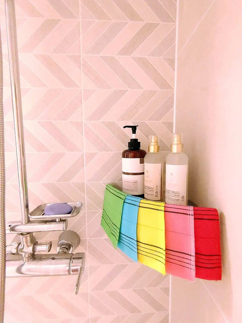 Korean Exfoliating Mitt Bath Washcloth For Back And Body Large 5 Colors hanging in shower with toiletries.