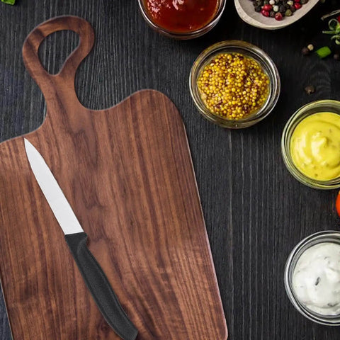 Wooden charcuterie board with knife and sauces on dark background