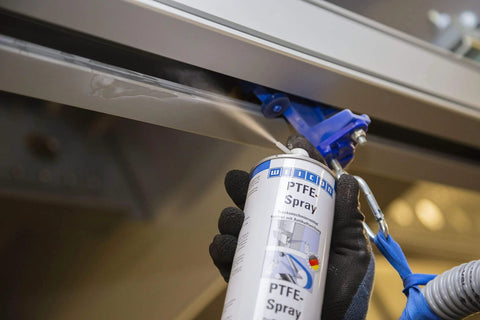 Applying grease-free dry PTFE lubricant spray for metal, plastic and wood surfaces, no-mess non-stick coating, industrial use.