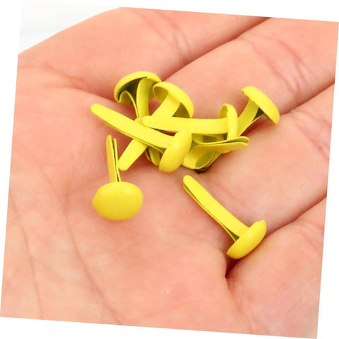Hand holding yellow metal brads from 500 Pieces Scrapbooking Paper Fasteners Brads Clip Set For Photos And Cards And Paper Crafts Durable Vintage