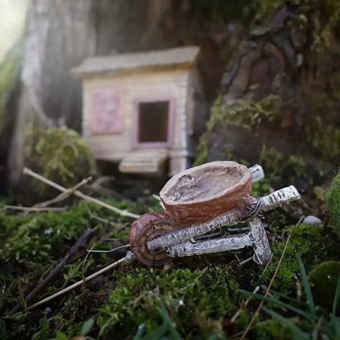 Totally Cute Mini Walnut Birch Tree Wheelbarrow For Fairy Garden And Outdoor Dollhouse Decor on mossy ground in front of tiny house