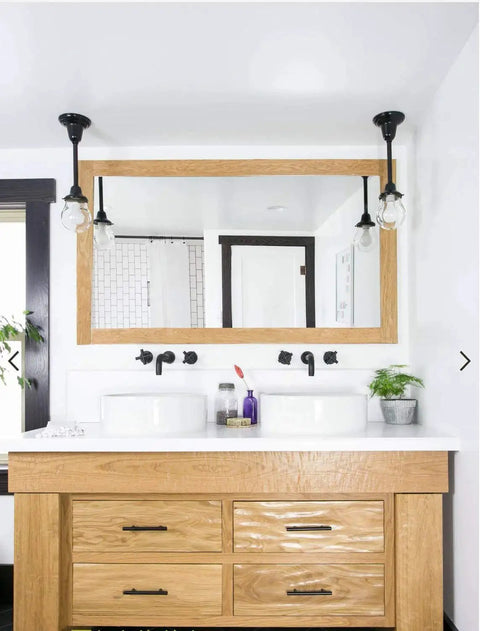 Modern bathroom with wooden vanity, dual sinks, black faucets, and wall lights, featuring a large rectangular mirror.