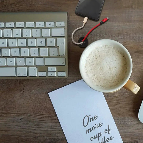 Overhead view of a desk setup with a cup of coffee, keyboard, smartphone, and cable organized with a silicone grommet.