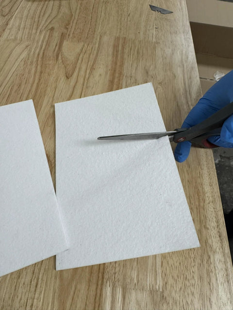 Two white CeraTex ceramic fiber paper sheets (1/8 in thick, 11 x 12 in) being cut with scissors.