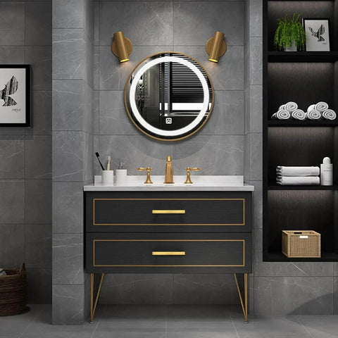 Modern bathroom with black vanity featuring gold cabinet pulls, round mirror, gold faucets, and grey tile walls.