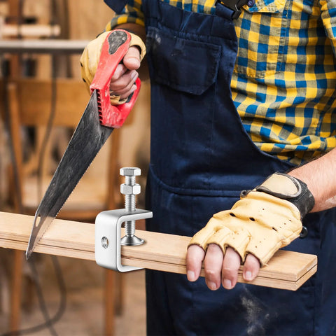 1-Inch stainless steel mini C-clamp gripping a wooden plank while a worker uses a handsaw in a workshop