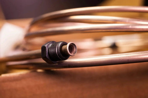Close-up of copper-nickel alloy brake line tube with a threaded fitting on a curved metal tube.