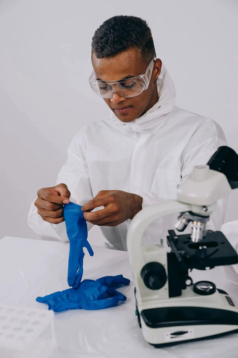 Scientist in lab coat handling Cobalt Blue Nitrile Examination Gloves Latex Free Medical Grade 4.5 Mil beside microscope.