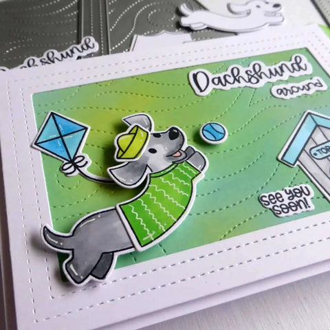 Handmade card featuring stitched rectangle frame die cuts, decorated with a dachshund illustration, kite, and playful sentiment on green background.