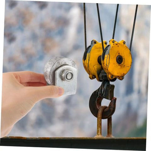 Hand holds a small metallic wheel next to a large industrial pulley system with yellow casings against a blurred background.